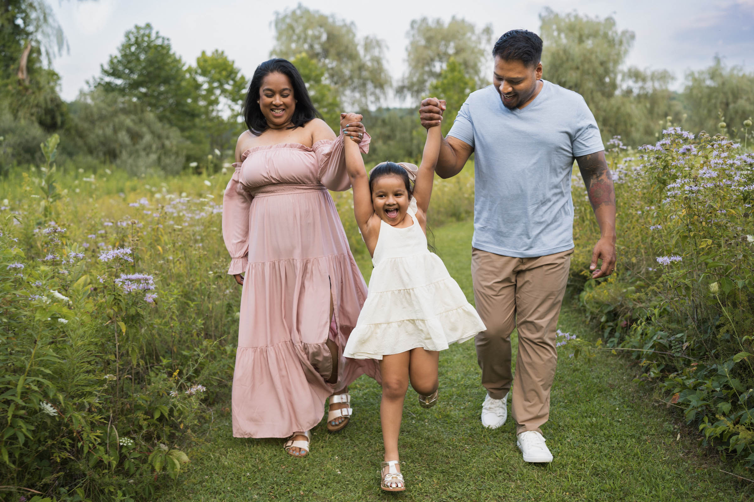 Girl being swung by the hands joyfully by parents outside in summertime