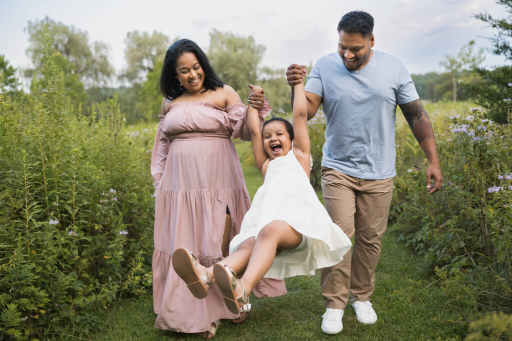 Girl being swung by the hands joyfully by parents outside in summertime and laughing