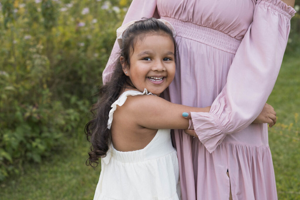 Little girl smiling while wrapping arms around mother's middle
