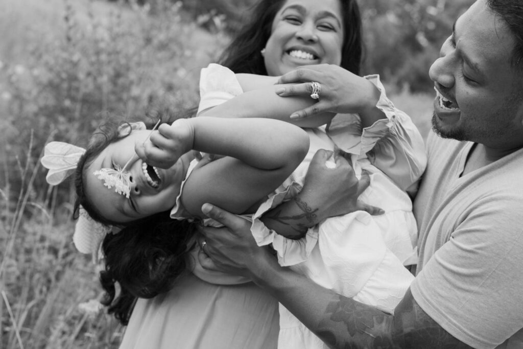 Girl joyfully being tipped over by parents with flower covering her face