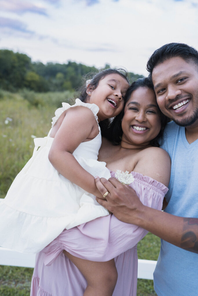 Family joyfully smiling at camera near white fence