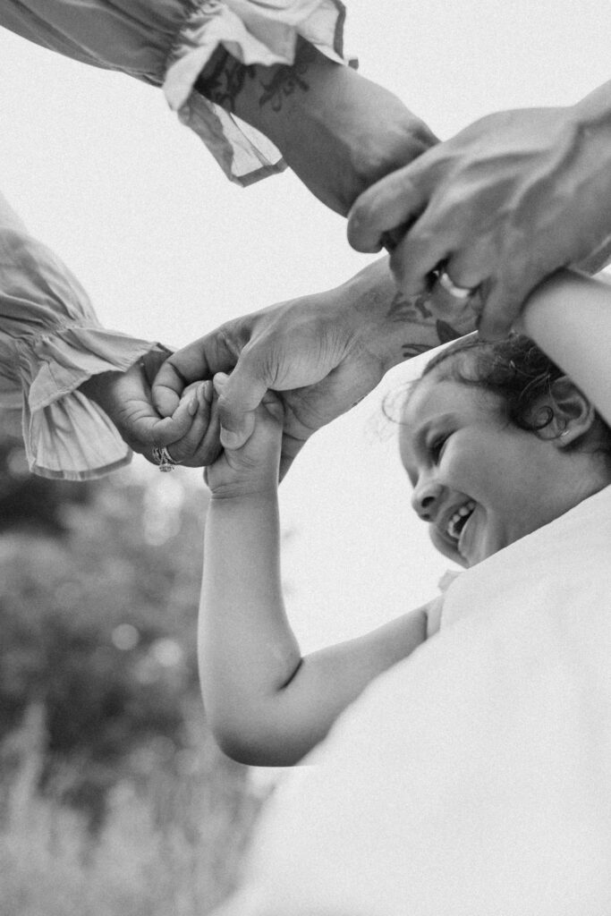 The hands of mother, father, and young daughter holding each other while girl smiles