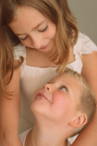 Young sister and brother sharing a tender moment and smiling at each other during an Oklahoma City in-home family session